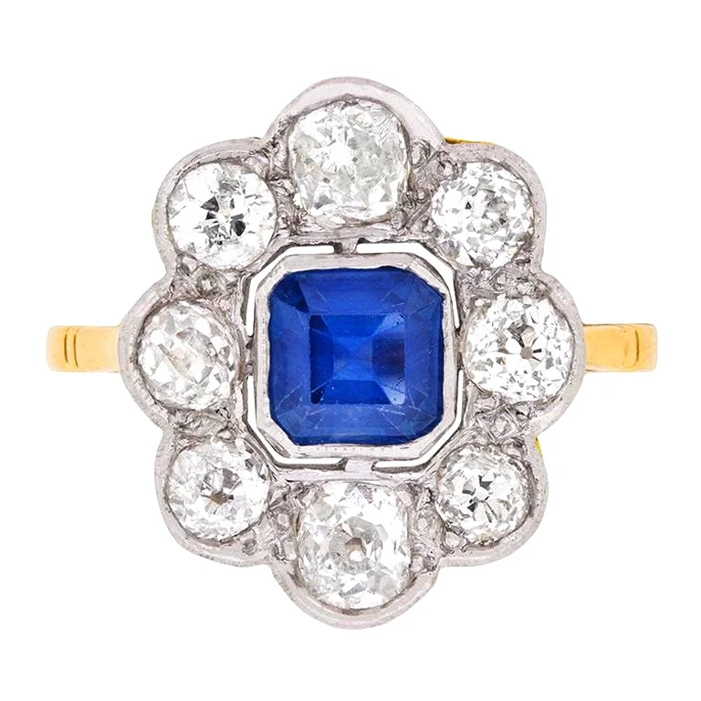 A 1920s Art Deco engagement ring featuring an Asscher cut sapphire at its center, wrapped in a border of old European-cut diamonds. Offered by Farringdons. 